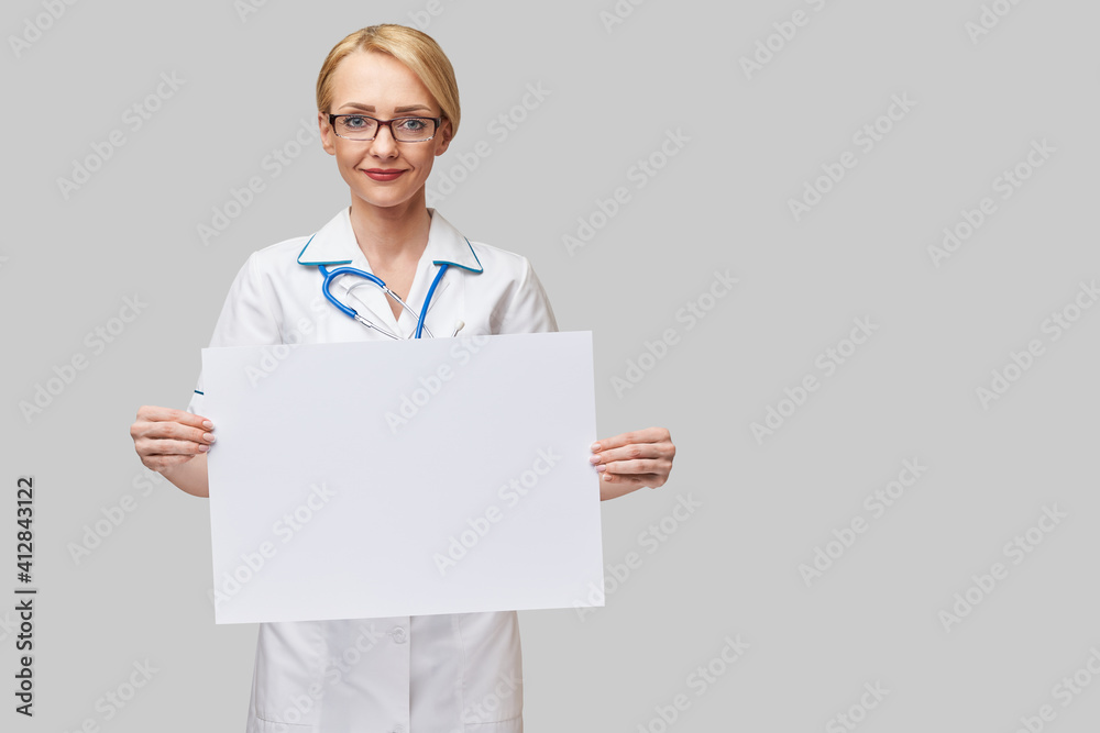 Female doctor holding a blank banner sign standing over grey background Female doctor holding a blank banner sign standing over grey background