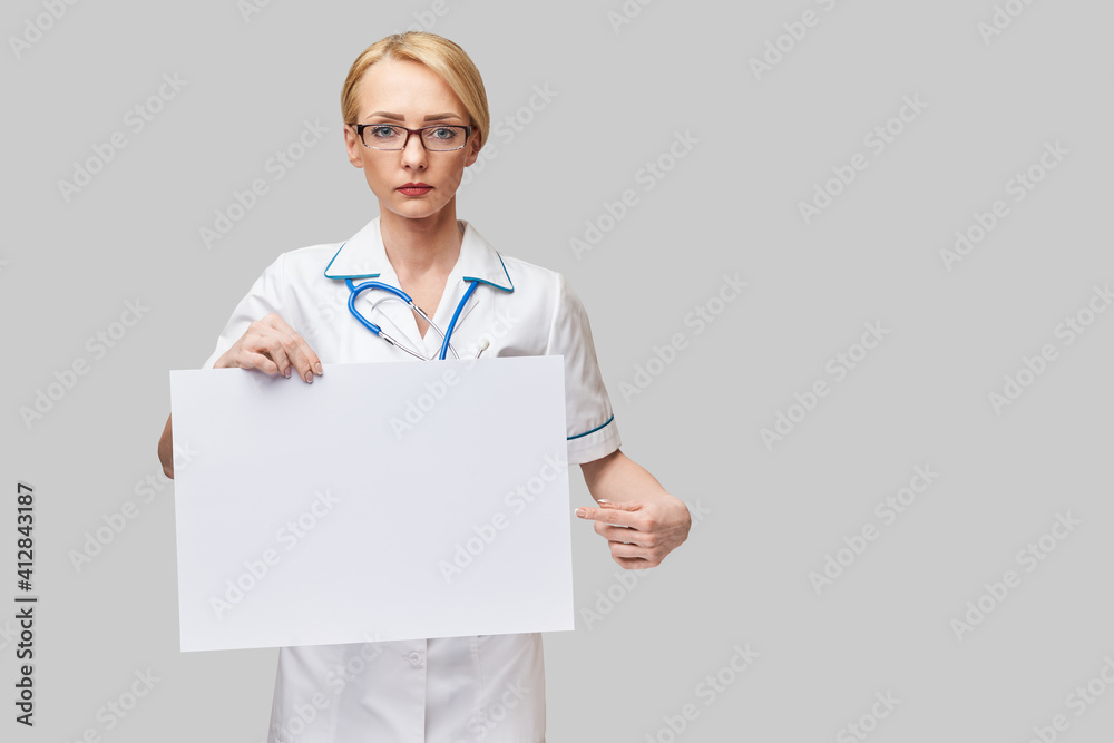 Female doctor holding a blank banner sign standing over grey background Female doctor holding a blank banner sign standing over grey background
