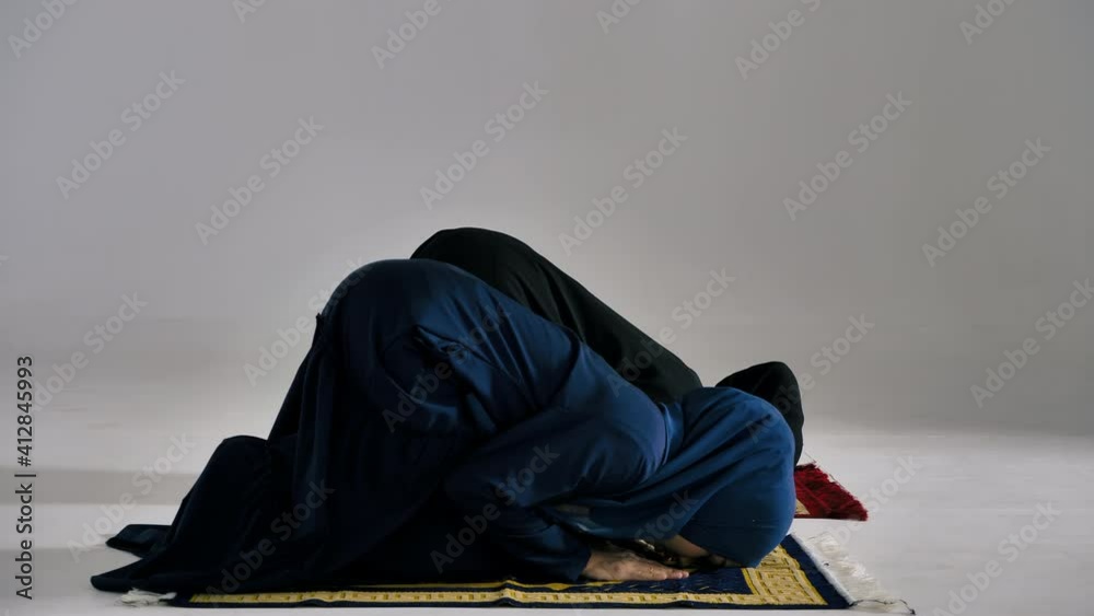 Two Asian Muslim young women in traditional hijab are praying glorify Allah and practicing the Islamic faith in mosque.
