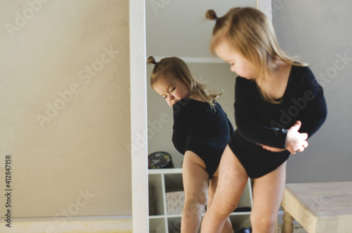 Funny little ballerina looking in mirror at home. Little girl dreams of becoming a ballerina, reflection in the mirror. Preparations for ballet or dance lessons. Selective focus. Hobbies for girl 