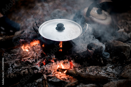 view of steaming iron pot with lid standing on the wood in fire.