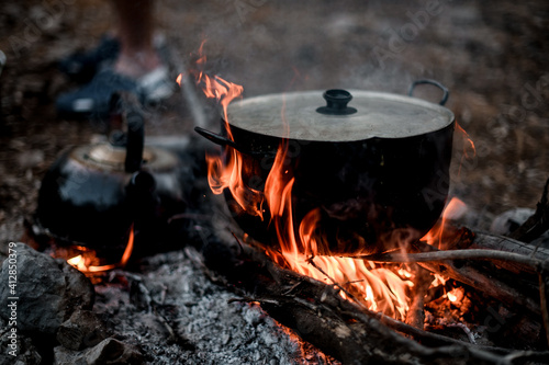 Close-up view of iron pot with lid standing on the wood in fire.