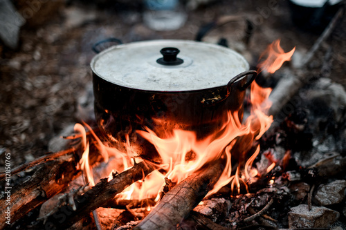 Close-up of iron pot with lid standing on the wood in fire.