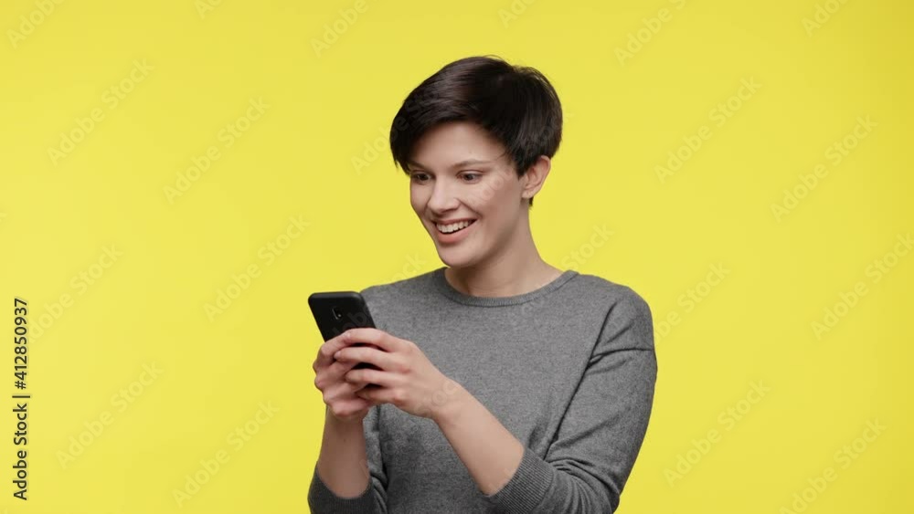 Color of the year 2021. Ultimate Gray and illuminating. Surprised young beautiful woman in gray sweatshirt using smartphone, get shocking and unbelievable news, isolated on yellow background. Color of the year 2021. Ultimate Gray and illuminating. Surprised young beautiful woman in gray sweatshirt using smartphone, get shocking and unbelievable news, isolated on yellow background.