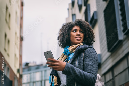 Attractive brunette girl with afro hair smiles while looking at mobile phone