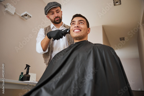 Delightful Caucasian hair stylist using modern machine in beauty salon