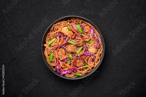 Pancit Bihon in black bowl on dark slate table top. Filipino cuisine noodles dish with pork belly, chicken, vegetables. Asian food. Top view