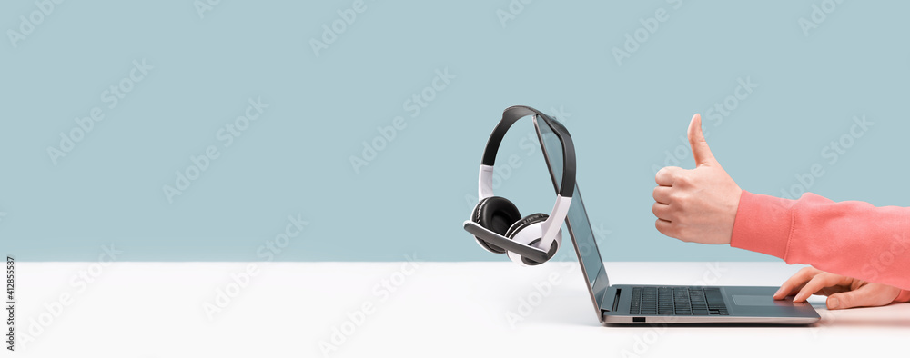 Side view of slim laptop and like thumb up hand. wireless headphones on grey desk. Blue background. Distant learning. working from home, online courses support. Audio podcast. vlogger blogger banner - obrazy, fototapety, plakaty 