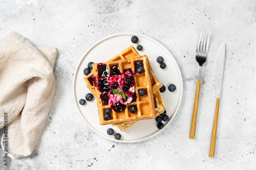 Obraz na płótnie Belgian or Brussels waffles with Greek yogurt and blueberry jam. Homemade waffles in a white plate on the light gray kitchen table. Traditional classic Belgian waffles. Top view w salonie