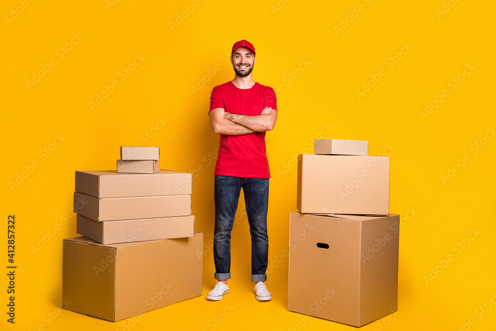 Full length body size photo happy courier with crossed hands packing delivery boxes isolated on vivid yellow color background Full length body size photo happy courier with crossed hands packing delivery boxes isolated on vivid yellow color background