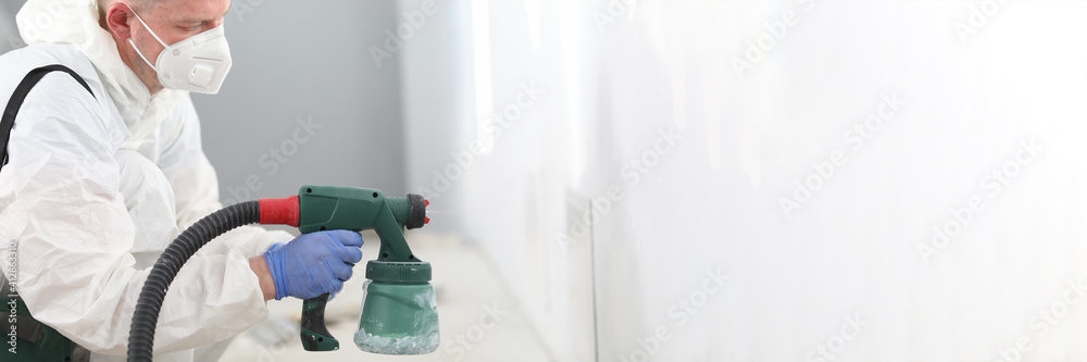 Man in mask holds spray gun in his hands and paints the wall. Courses on mastering new profession concept Man in mask holds spray gun in his hands and paints the wall. Courses on mastering new profession concept