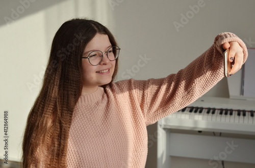 Cute girl in a pink sweater takes a selfie. She has long brown hair. Shes wearing fancy glasses.
