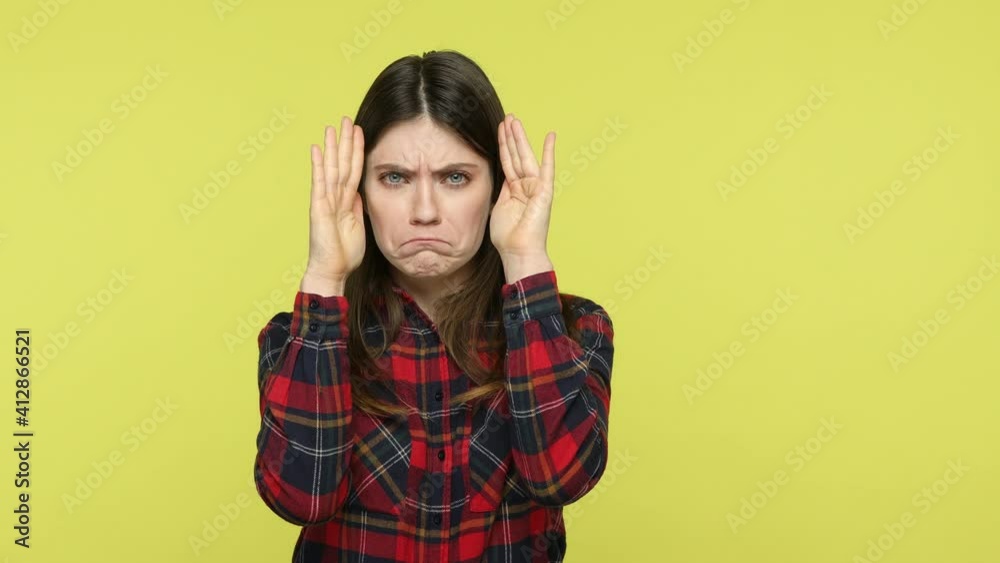 Brunette woman in checkered shirt closing face with hands and showing different facial emotions, surprise, sadness, joy, practicing acting skills. Indoor studio shot isolated on yellow background Brunette woman in checkered shirt closing face with hands and showing different facial emotions, surprise, sadness, joy, practicing acting skills. Indoor studio shot isolated on yellow background