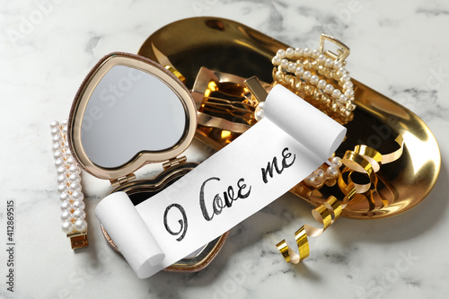 Paper with handwritten phrase I Love Me, mirror and hair accessories on table, closeup