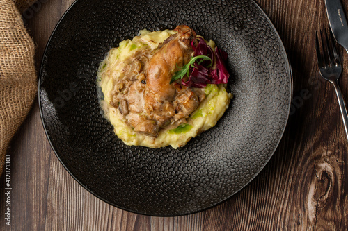 Фотография Baked meat and mashed potatoes served with mushrooms, green sauce and lettuce in black bowl
