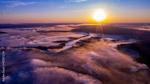 Aerial view of a beautiful summer landscape with a fog while dawn. Photo from drone of a foggy landscape in spring. Top view to land while sunrise. Sun is above the horizon