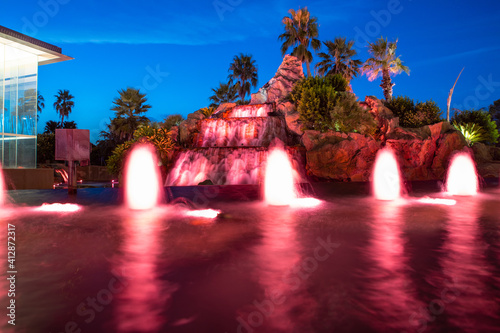 Colourful water fountain at night dark blue skies green palms 