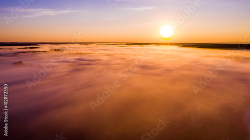 Aerial view of a beautiful summer landscape with a fog while dawn. Photo from drone of a foggy landscape in spring. Top view to land while sunrise. Sun is above the horizon