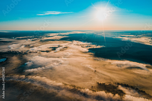 Fototapeta Naklejka Na Ścianę i Meble -  Aerial  view of a beautiful summer  landscape with a fog while dawn.  Photo from drone of a foggy landscape in spring. Top view to land while sunrise. Sun is above the horizon