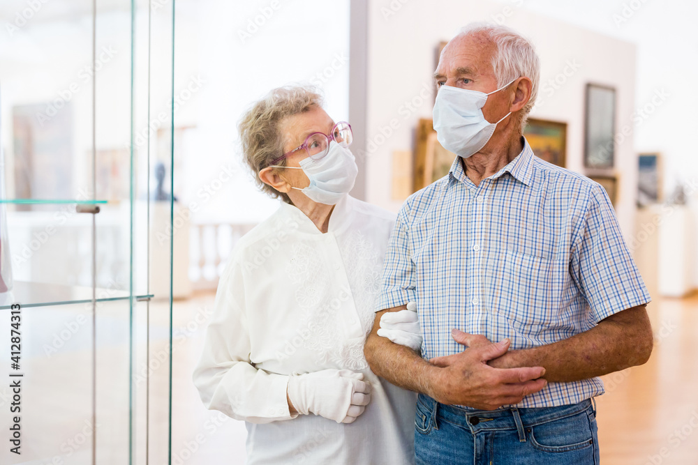 Obraz premium mature couple in mask protecting against covid examines paintings on display in hall of art museum