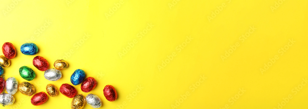 Chocolate eggs wrapped in colorful foil on yellow background, flat lay with space for text. Banner design Chocolate eggs wrapped in colorful foil on yellow background, flat lay with space for text. Banner design