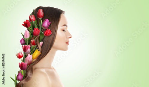 Pretty woman wearing beautiful wreath made of flowers on light green background, space for text