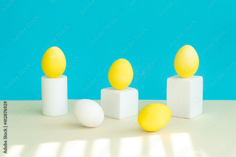 Obraz premium In the foreground lies a yellow egg in the background is geometric figures, on a pedestal, there are yellow eggs. Selective focus.