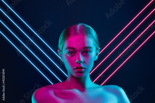 Future. Portrait of female fashion model in neon light with neoned blue glowing lines on dark studio background. Beautiful woman with trendy make-up and well-kept skin. Vivid style, beauty concept.