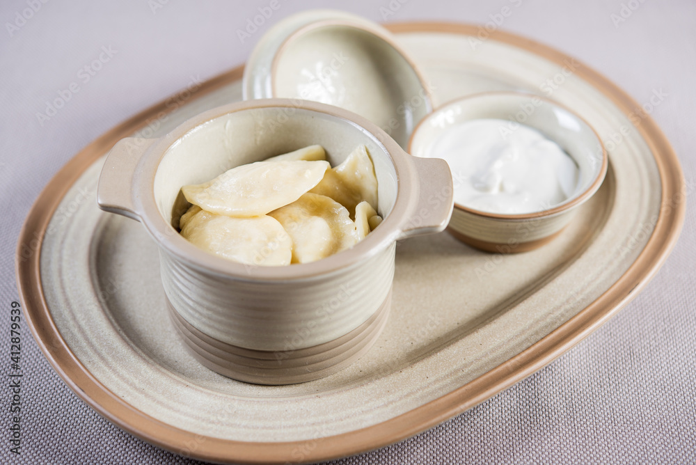 portion of ukrainian russian polish dumplings stuffed with potato in a ceramic pot served with sour cream portion of ukrainian russian polish dumplings stuffed with potato in a ceramic pot served with sour cream