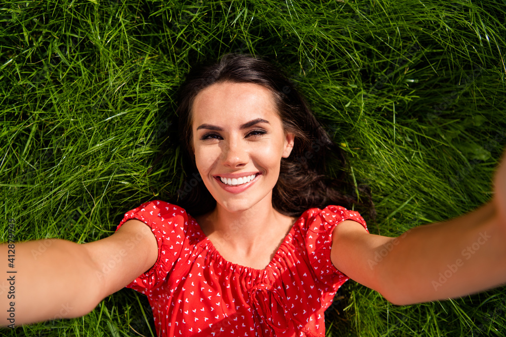 Photo of cute adorable young woman dressed red off-shoulders dress relaxing green grass making selfie outdoors backyard Photo of cute adorable young woman dressed red off-shoulders dress relaxing green grass making selfie outdoors backyard