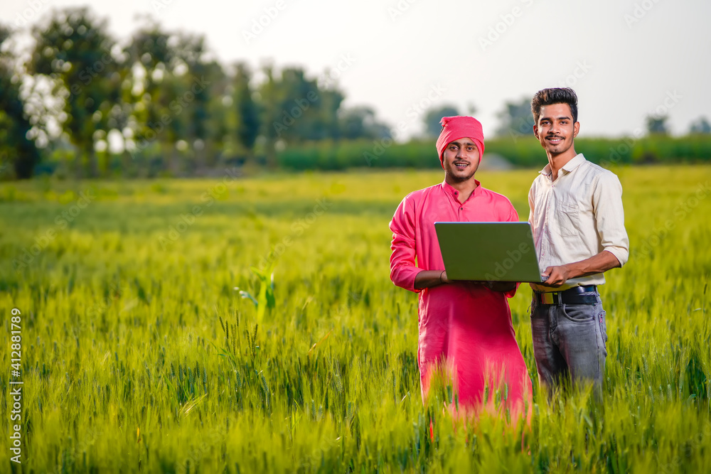 Young indian agronomist and farmer using laptop for seeing some information about farming Young indian agronomist and farmer using laptop for seeing some information about farming