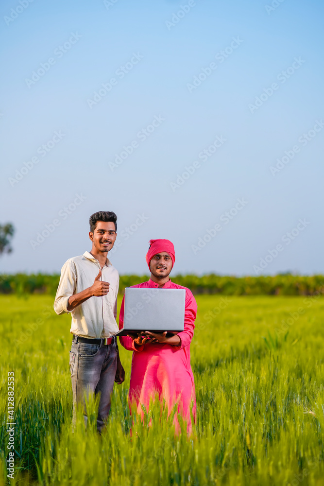 Young indian agronomist and farmer using laptop for seeing some information about farming Young indian agronomist and farmer using laptop for seeing some information about farming