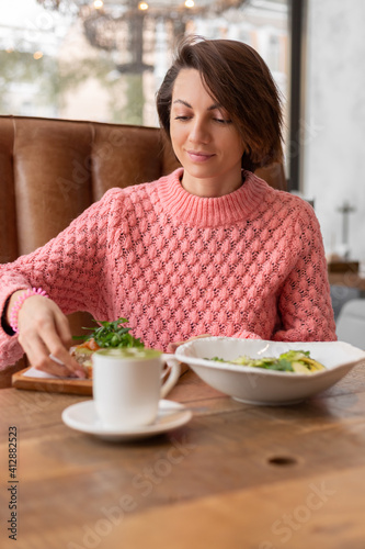 Woman in a restaurant in a cozy warm sweater eating healthy breakfast toast with arugula and salmon