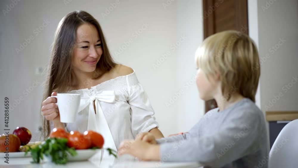 Portrait of beautiful loving mother touching blond hair of little cute son in the morning at home. Smiling Caucasian woman enjoying breakfast with boy. Love and family lifestyle. Portrait of beautiful loving mother touching blond hair of little cute son in the morning at home. Smiling Caucasian woman enjoying breakfast with boy. Love and family lifestyle.