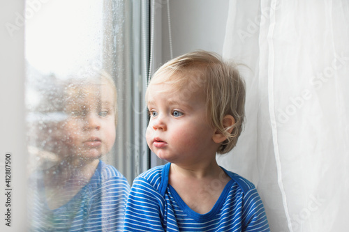 Wallpaper Mural Little sad caucasian child looking throw at home on window in rainy day. Stay home coronavirus concept. Torontodigital.ca