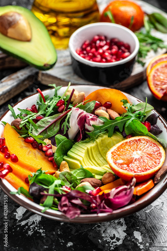 Buddha bowl dish with avocado, persimmon, blood orange, nuts, spinach, arugula and pomegranate. Healthy balanced eating. Top view. vertical image