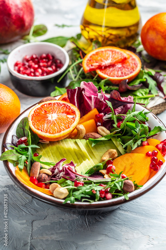 Vegan, detox Buddha bowl with avocado, persimmon, blood orange, nuts, spinach, arugula and pomegranate. Healthy balanced eating. Top view. vertical image