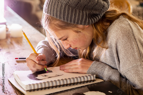 Teenage girl in a woolly hat drawing with a pencil on a sketchpad. photo