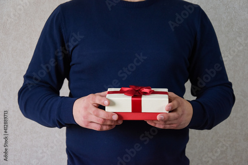 A man holds a gift box with a red bow. Man's hands are holding a surprise. photo
