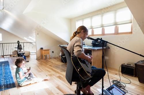 Teenage girl playing her guitar and singing, her brother playing in the background
