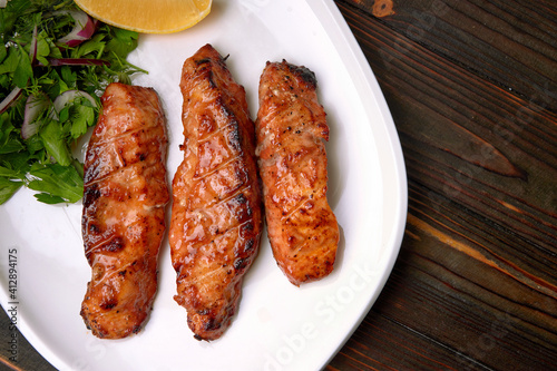 Three grilled pieces of salmon fillet, trout, with herbs and lemon, on a white plate, on a wooden background