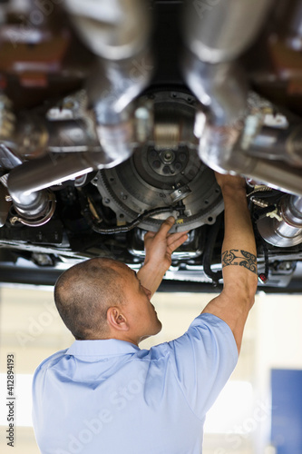 Pacific Islander mechanic works on the underside of a vehicle on a lift in an auto repair shop