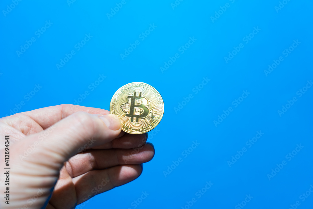 hand of an adult holds bitcoin coin. bitcoin cryptocurrency on blue background hand of an adult holds bitcoin coin. bitcoin cryptocurrency on blue background