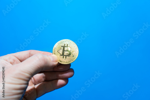 hand of an adult holds bitcoin coin. bitcoin cryptocurrency on blue background