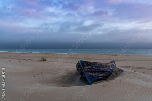 wreck of an old wooden rowboat buried in the sand with a beautiful sunset sky and ocean behind