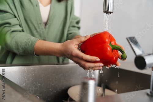Caucasian young woman washing bell pepper at home kitchen
