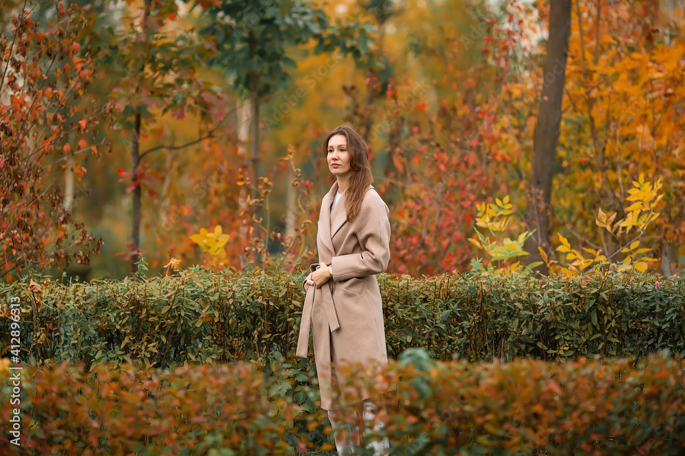 A girl with a Euro-Asian appearance in a pink coat and blue jeans with holes sits on a bench made of gray unpainted boards in a park A girl with a Euro-Asian appearance in a pink coat and blue jeans with holes sits on a bench made of gray unpainted boards in a park
