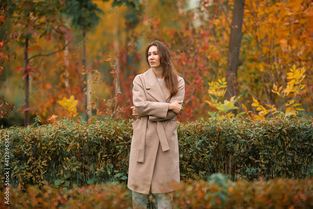 A girl with a Euro-Asian appearance in a pink coat and blue jeans with holes sits on a bench made of gray unpainted boards in a park A girl with a Euro-Asian appearance in a pink coat and blue jeans with holes sits on a bench made of gray unpainted boards in a park
