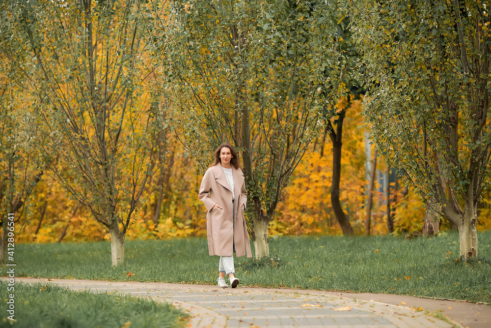 Fototapeta premium A Caucasian girl in a pink coat and blue jeans with holes dances in an autumn park