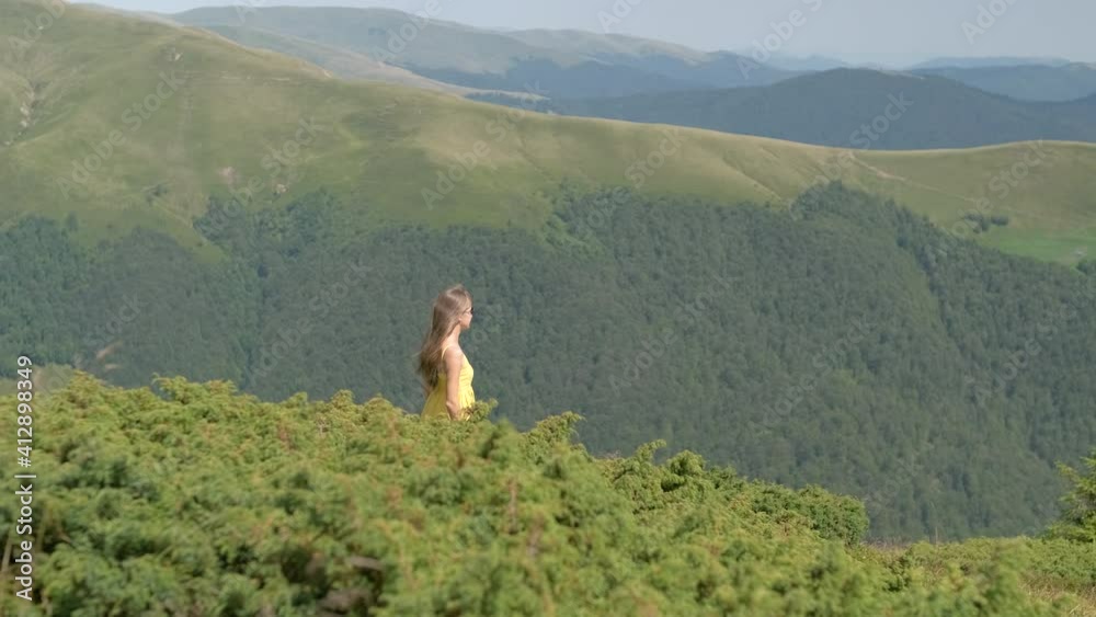 Young happy woman in yellow dress walking on grass field on a windy day in summer mountains. Young happy woman in yellow dress walking on grass field on a windy day in summer mountains.
